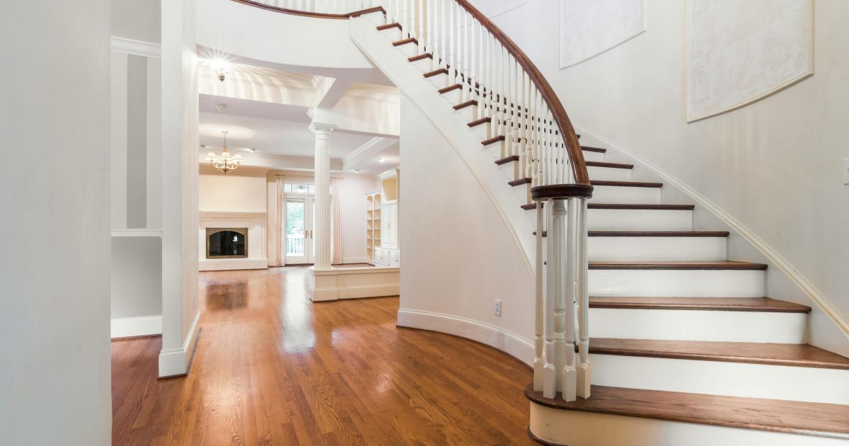 White curved staircase with a wooden handrail in a home with hardwood floors